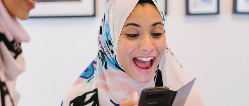 woman in hijab reading a blog post on her cell phone and smiling